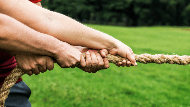 A high-performance team working together as symbolised by multiple people pulling one side of a rope in a tug of war